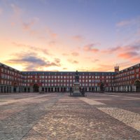 Madrid, Spain - April 30, 2018:  Overview of Plaza Mayor (English Main Square) during sunrise.
The Plaza Mayor was first built (1580–1619) during Philip III's reign and is a central plaza in the city of Madrid; is rectangular in shape and is surrounded by three-story residential buildings having 237 balconies facing the Plaza. It has a total of nine entrance ways. The Casa de la Panadería (Bakery House), serving municipal and cultural functions, dominates the Plaza Mayor.
There is a bronze statue of King Philip III at the center of the square, created in 1616 by Jean Boulogne and Pietro Tacca.
The Plaza Mayor represents the work of Juan de Villanueva, one of Spain’s most famous neoclassical architects, who managed to reconstruct it after several fires suffered over the years.